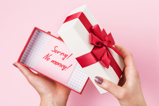 Girl opens a box with a gift on a pink background, top view. Concept on the topic of lack of money to buy gifts