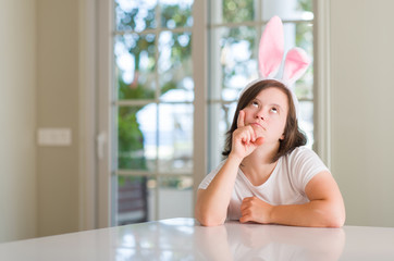 Down syndrome woman at home wearing easter rabbit ears serious face thinking about question, very...