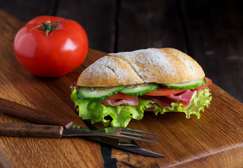 Whole sandwich on wooden board with tomato