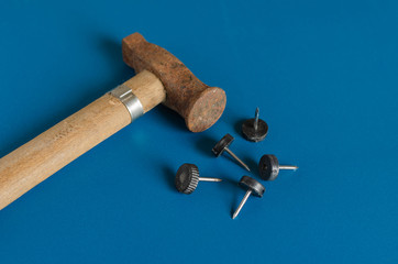 Old hammer and furniture nails on a blue background. A small rusty hammer and five nails. Side...