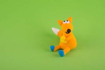 Cute toy fox made of bright colorful clay holding piece of cheese and sitting on green background