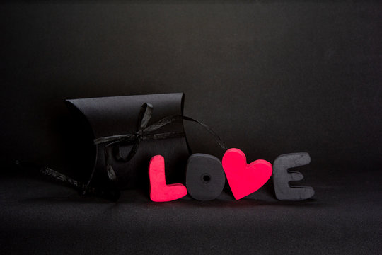 Black gift box and red word LOVE on dark background, copy space. Valentine's day, birthday romantic concept, greeting card.