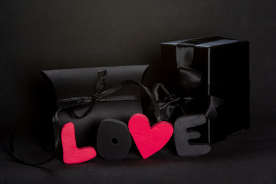 Black gift box and red word LOVE on dark background, copy space. Valentine's day, birthday romantic concept, greeting card.
