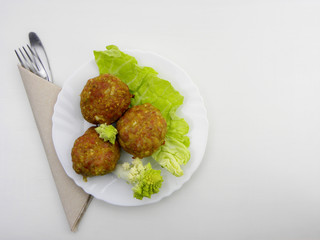 Homemade meatballs on a white plate with lettuce and romanesco cabbage on a white background