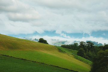 Green meadows, clouds flying low above the ground, clouds and small village houses in the French pyrenees on a bright summer sunny day. Mountain life, calm and solitude. Camino de Santiago landscapes.