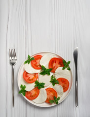 Fresh salad with tomatoes, mozzarella and basil on white plate on light wooden background. Copy space. 