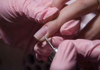 The manicurist cleans the cuticle of the nails with the device. Cuticle removal using a machine with a cutter. Professional manicure in the salon close-up.