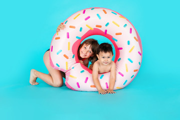 Happy baby boy and elder sister in swimsuit with swimming ring donut on a colored blue background