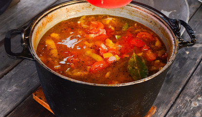A soup of tomatoes and red pepper in a large black saucepan. Close-up.