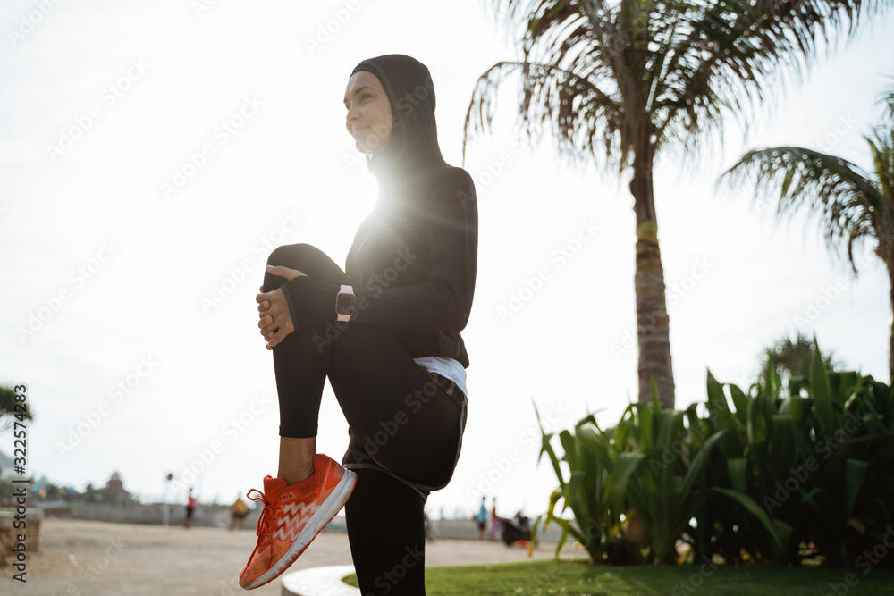 Wall mural young fitness muslim woman runner stretching legs before run