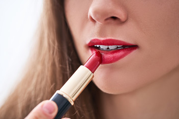 Female applying classic bright matte red lipstick on her lips close up