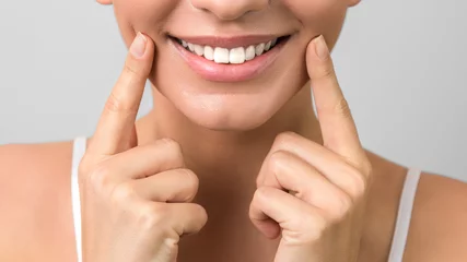 Tableaux sur Plexiglas closeup beautiful healthy smile and white teeth of a young attractive woman on grey background
