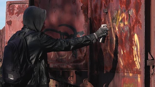 Homeless man spray painting old train wagon with aerosol can