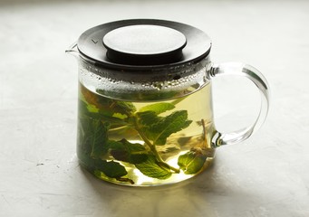 Glass teapot with green tea with mint on a light gray background