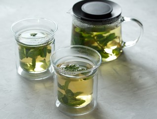 Two glass cups with green tea with mint on a light gray table