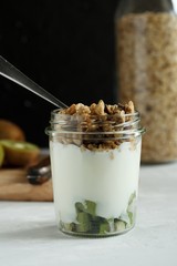 Natural yogurt with granola and kiwi in a glass jar on a light gray table and on a black background