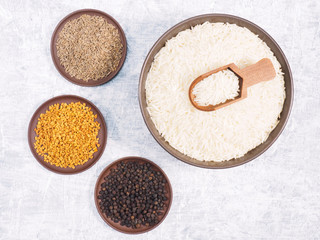 Spice black pepper, fenugreek, cumin (jeera) for long grain Basmati rice in bowl, scoop, clay plate on white concrete background