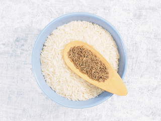 Indian long grain Basmati rice in blue ceramic bowl, cumin (jeera) on white concrete background