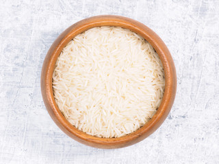 Indian long grain Basmati rice in brown wooden bowl on white concrete background