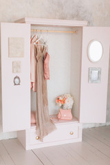 wooden pink wardrobe for women’s clothes, open doors, decor, mirror, bag, hangers, silk dresses in a bright room, concept, flowers delicate pastel colors