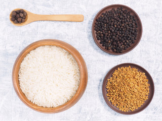 Indian long grain Basmati rice in brown wooden bowl, fenugreek, black pepper, allspice on white concrete background