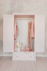 wooden pink wardrobe for women’s clothes, open doors, decor, mirror, bag, hangers, silk dresses in a bright room, concept, flowers delicate pastel colors