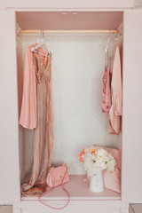 wooden pink wardrobe for women’s clothes, open doors, decor, mirror, bag, hangers, silk dresses in a bright room, concept, flowers delicate pastel colors
