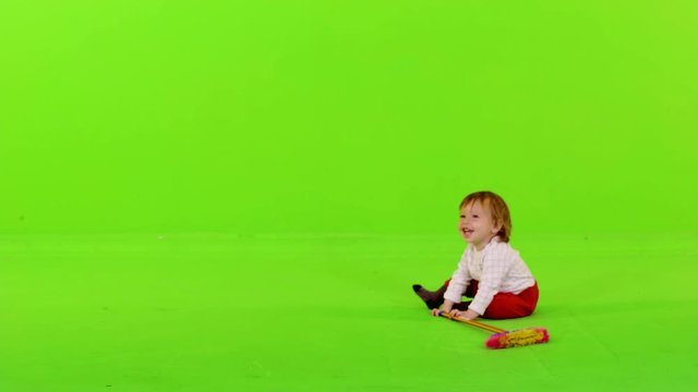 Little toddler standing and walking, holding a broom, over green screen.