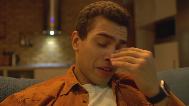 Upset young man crying and drinking alcohol alone, suffering depression crisis