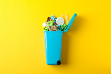 Recycle bin with trash on yellow background, space for text
