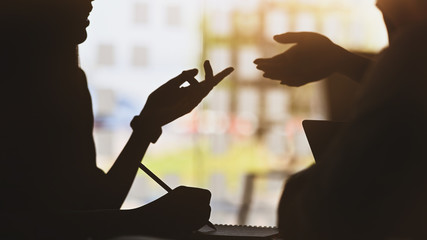 silhouette of young designer team standing with a white blank screen laptop and notebook in hands...