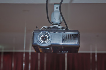 A white overhead projector on ceiling indoors. Modern video projector on ceiling in room . Black...