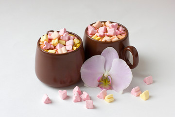 Brown cups of hot cocoa with marshmallows in heart shape on white background.