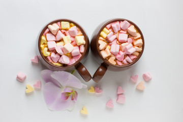 Top view of brown cups of hot cocoa with marshmallows in heart shape on white background.