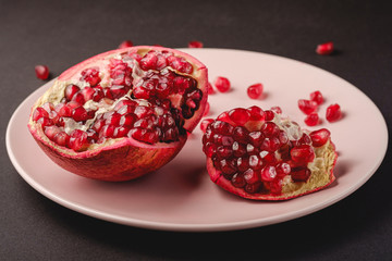Fresh tasty sweet peeled pomegranate with red seeds in pink plate on dark black background, angle...