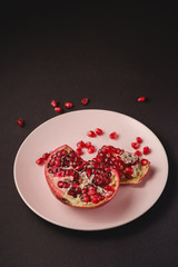 Fresh tasty sweet peeled pomegranate with red seeds in pink plate on dark black background, angle view, healthy food fruits