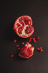 Fresh tasty sweet peeled pomegranate with red seeds on dark black background, angle view, selective focus, healthy food fruits
