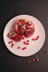 Fototapeta na wymiar Fresh tasty sweet peeled pomegranate with red seeds in pink plate on dark black background, top view, healthy food fruits