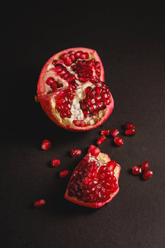 Fresh tasty sweet peeled pomegranate with red seeds on dark black background, angle view, selective focus, healthy food fruits