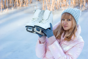 beautiful young woman in winter clothes holds curly white skates in the hands of a winter...