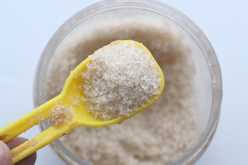 top view of raw sugar on plastic spoon on white background 