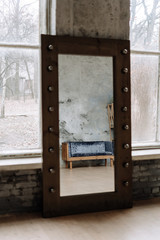 Ancient Wooden Couch Reflection in Vintage Mirror with Metallic Frame. Old Sofa with Velour Textile Cover, Grunge Brick and Stone Wall and Windows on Background. Loft Style Interior Vertical Photo