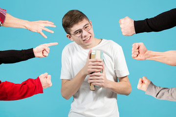 nerd with fear and caution looks at the camera, squinting and holding books to himself. Blue...