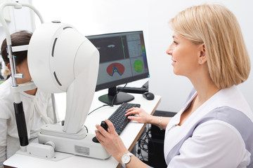 Optometrist woman checks girl eyesight. Diagnosis of eye anterior segment and tomography of boy...