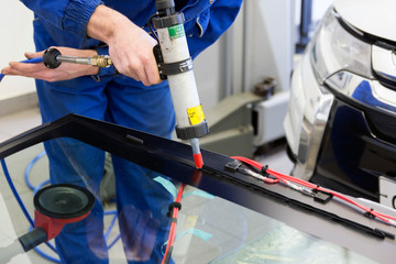 Automotive glass professional mechanic with a tool in the hands applies glue. Replacing broken...
