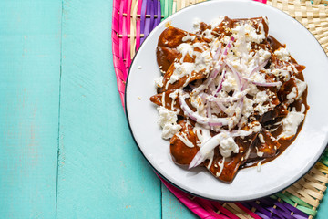 Mexican chilaquiles with mole sauce and fresh cheese on turquoise  background