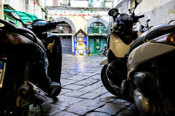 zwei Mofas Motorroller stehen auf einem gepflastertem Innenhof mit einer religiösen Gedenkstätte...