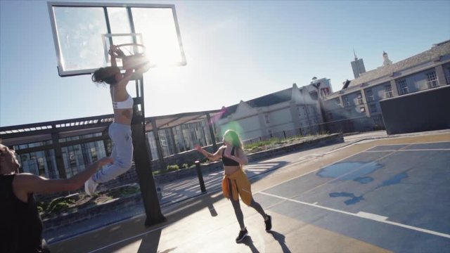 Group of friends playing street basketball and giving high five to one another. Man lifting woman to make a slam dunk while playing basketball game.