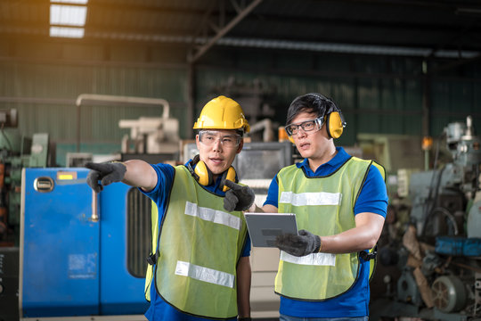 Industrial Engineers In Safety Uniforms Wearing Yellow Safety Helmets Are Inspecting Work By Tools.  And On The Job Training He Works In Industrial Machinery.