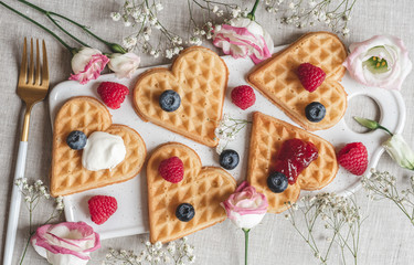 Homemade Belgian heart waffles with strawberry sauce and berries, pink flowers, spring, woman day morning concept, Valentine's day